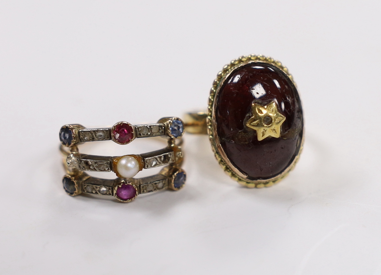 A late Victorian yellow metal, ruby sapphire, diamond and seed pearl set half hoop triple shank ring, size K, together with a Victorian yellow metal, cabochon garner and rose cut diamond set oval ring(a.f.), gross weight